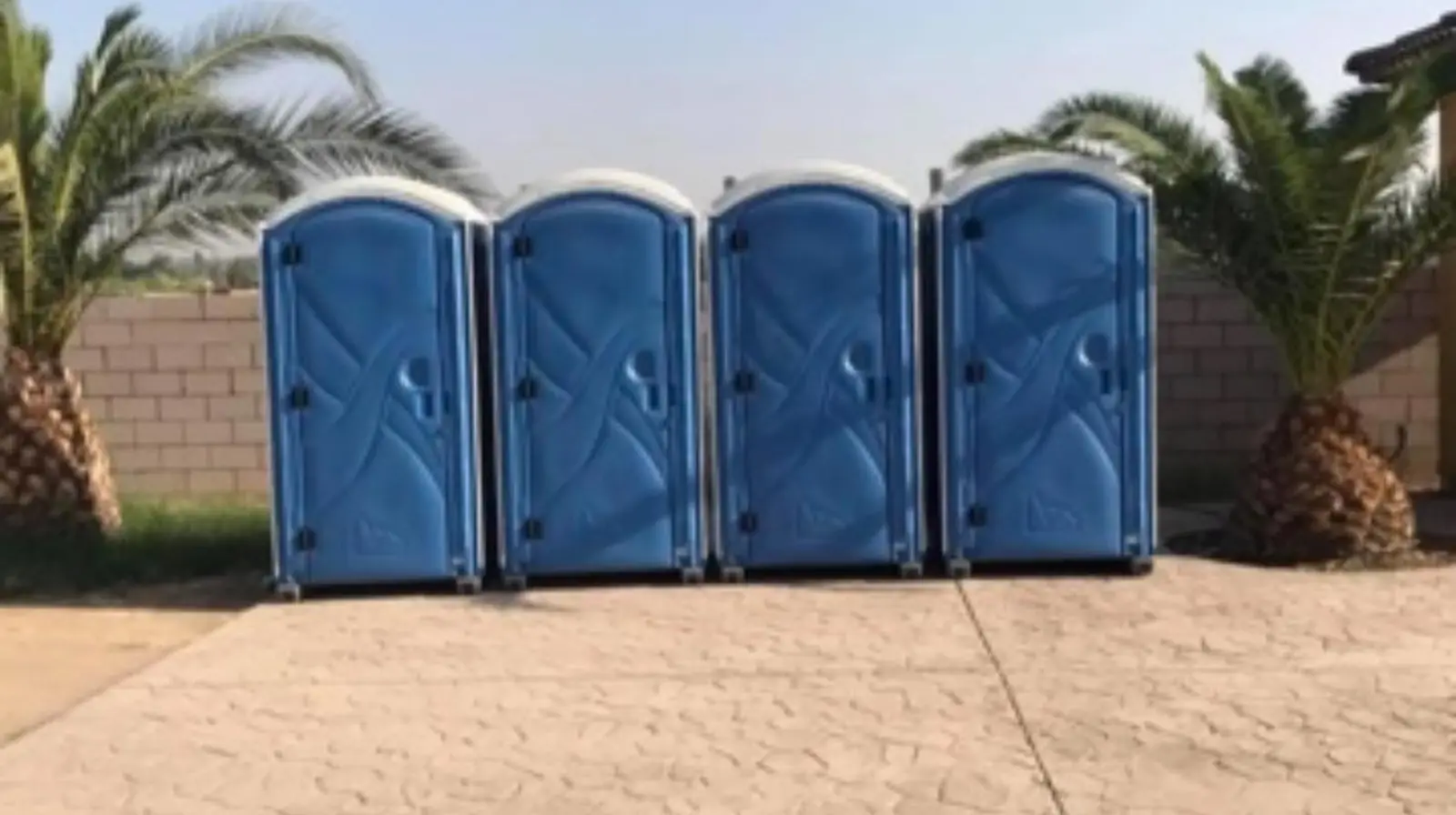 Four blue portable toilets lined up on a concrete pad for an event
