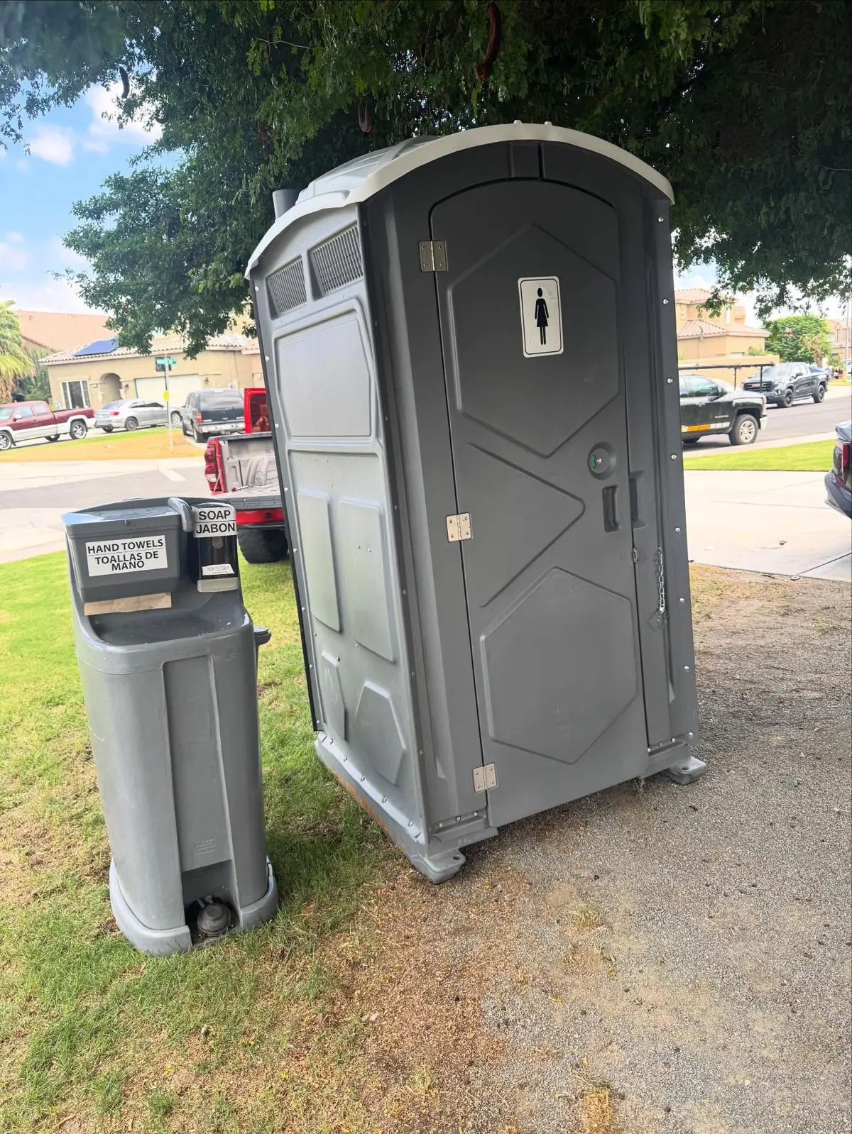 Portable toilet with a free-standing hand-wash station on grass