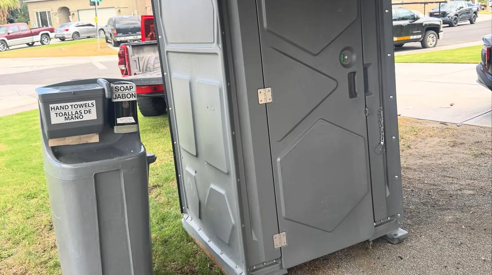 Gray portable toilet with a free-standing hand-wash station on grass