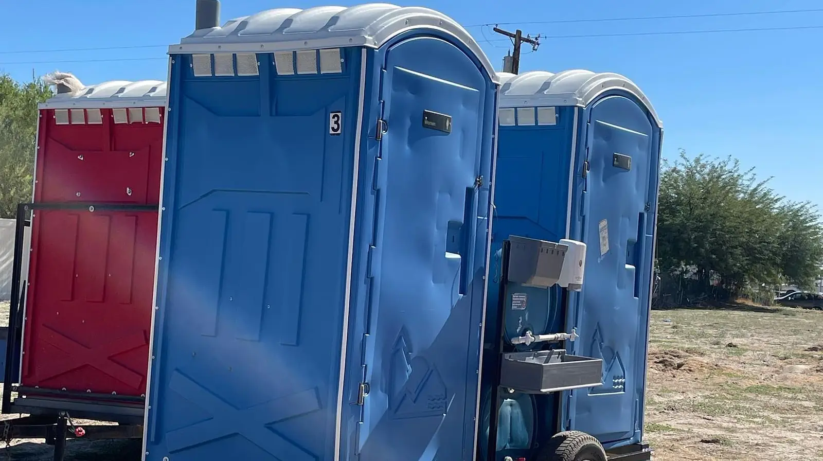 Trailer-mounted porta potties on open ground under a big blue sky