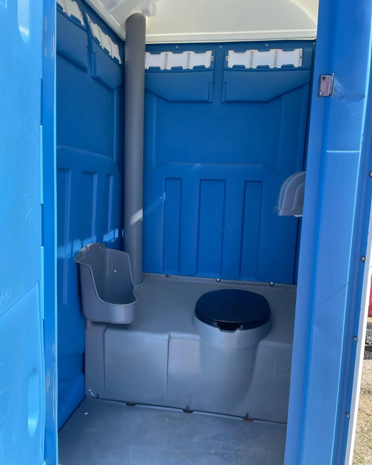 The urinal mounted on the wall of a standard portable toilet.