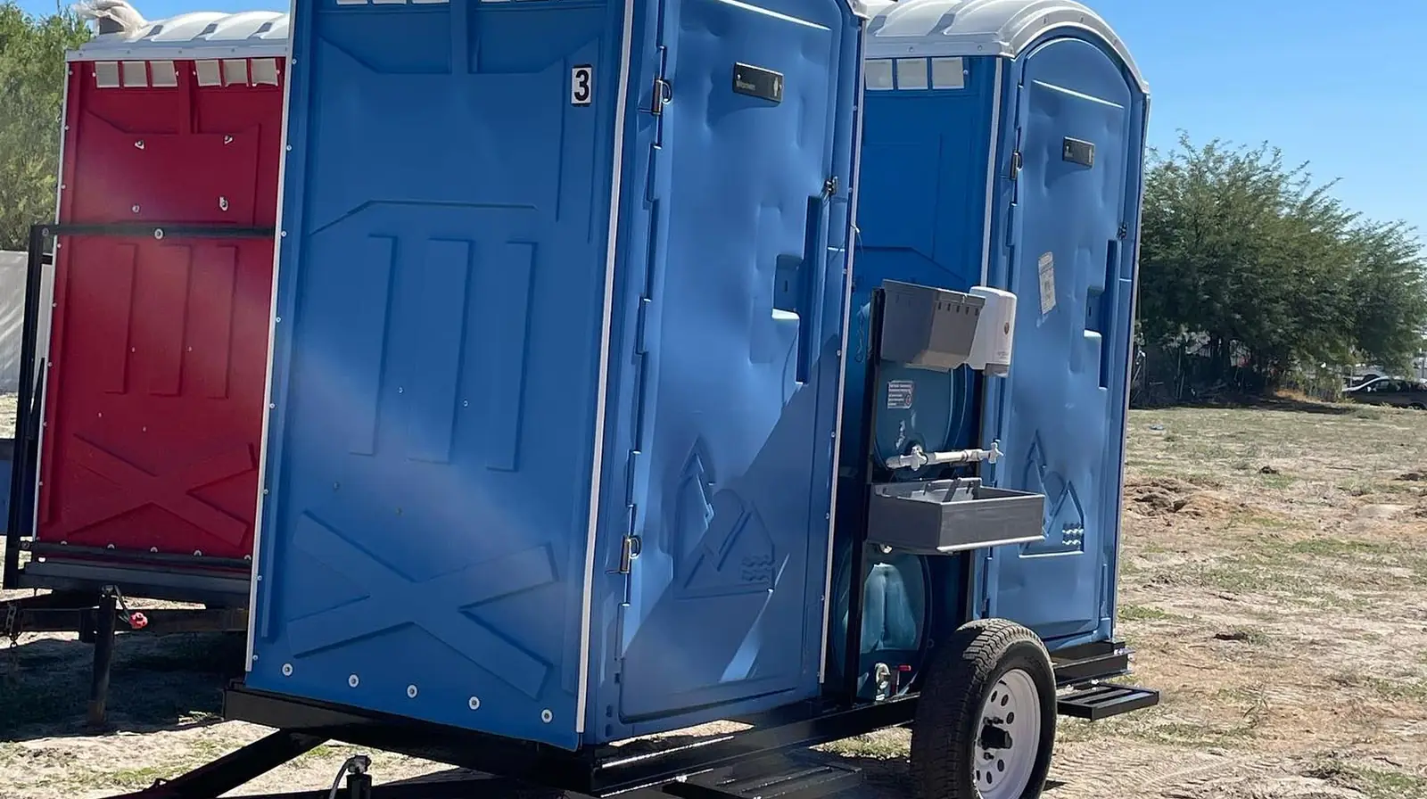 Blue towable portable toilet on a small trailer, with more units behind it