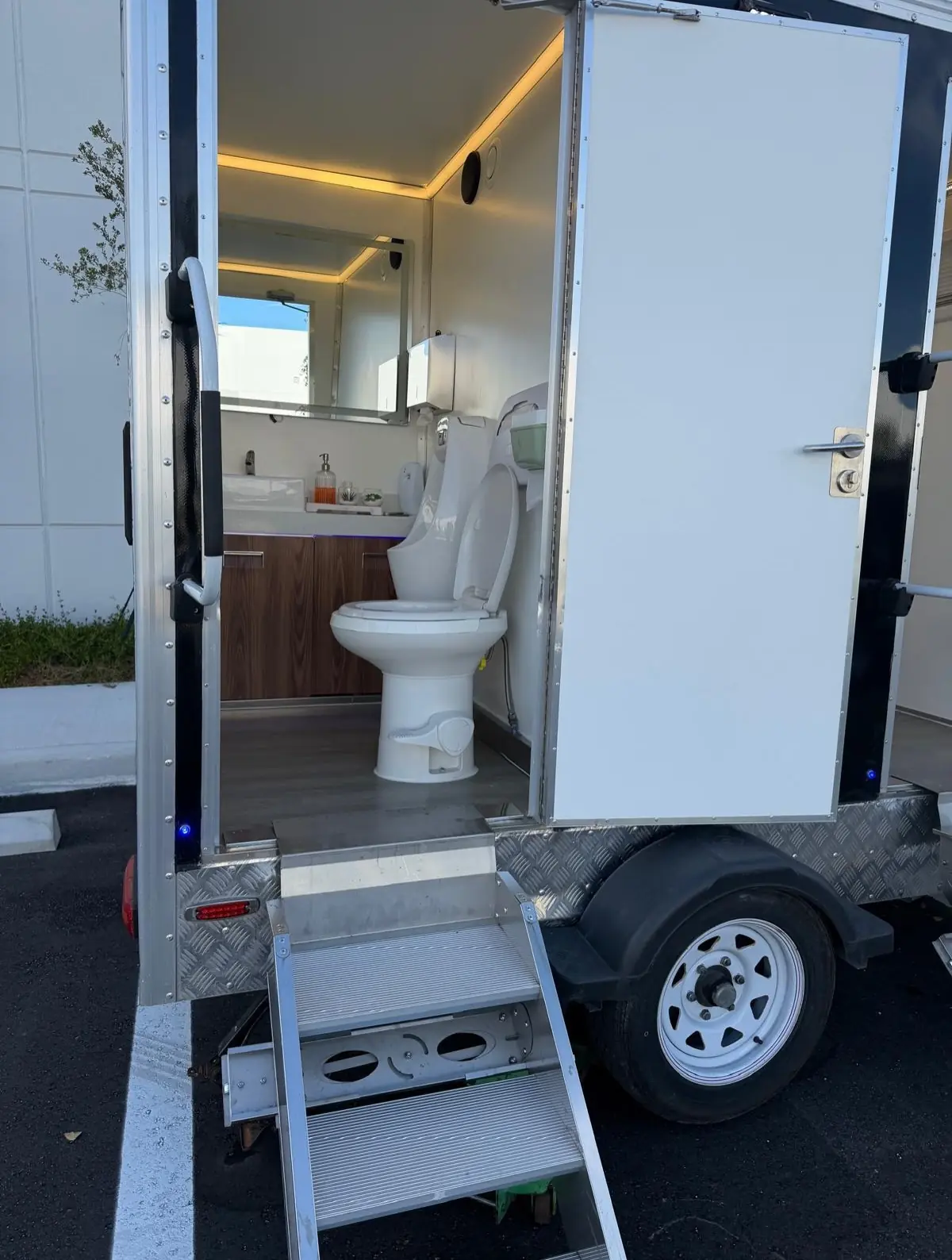 Inside a restroom trailer stall with a porcelain toilet and wall lighting.