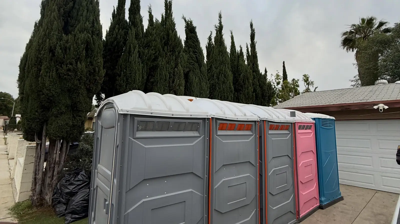 A row of gray and colored portable toilets lined up beside a driveway